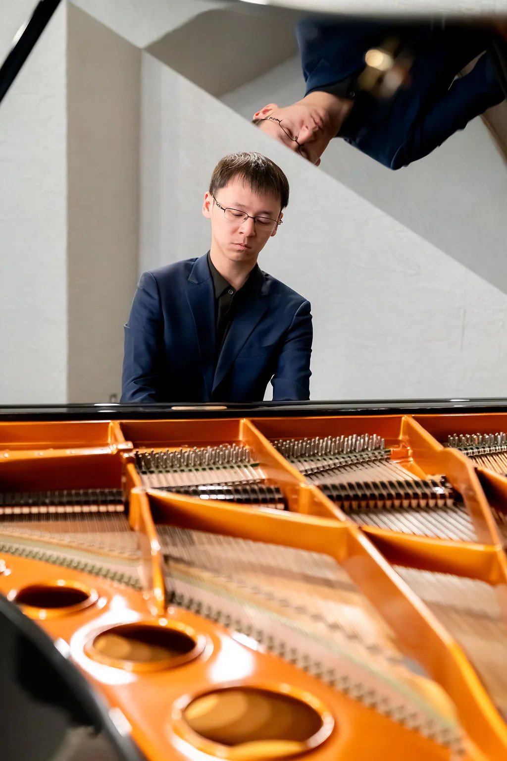 An advanced student reflected in the lid of the grand piano.